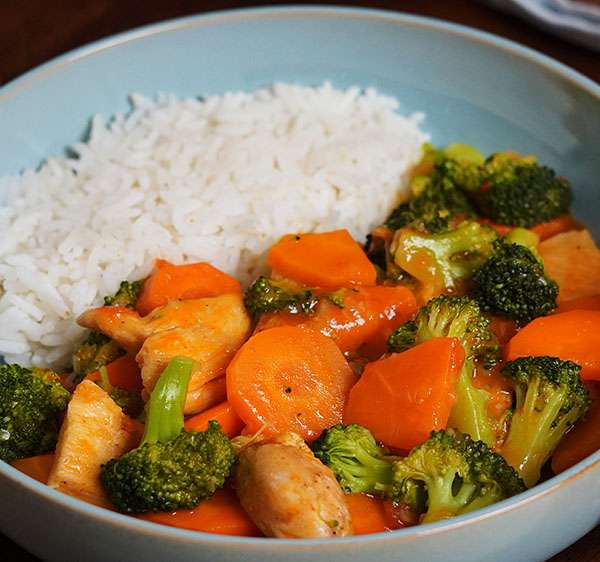 Plato de brócoli con pollo jugoso, acompañado de zanahorias y salsa cremosa, servido con arroz blanco