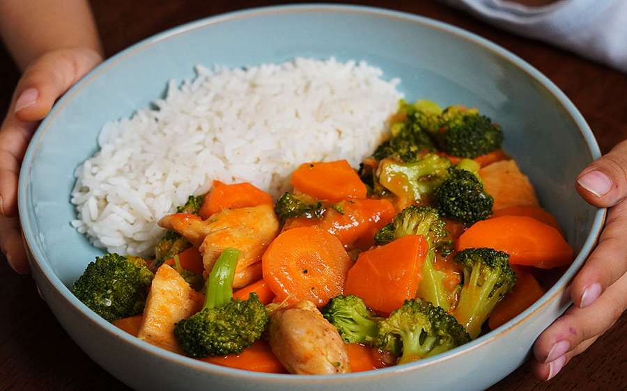 Plato de brócoli con pollo jugoso, acompañado de zanahorias y salsa cremosa, servido con arroz blanco