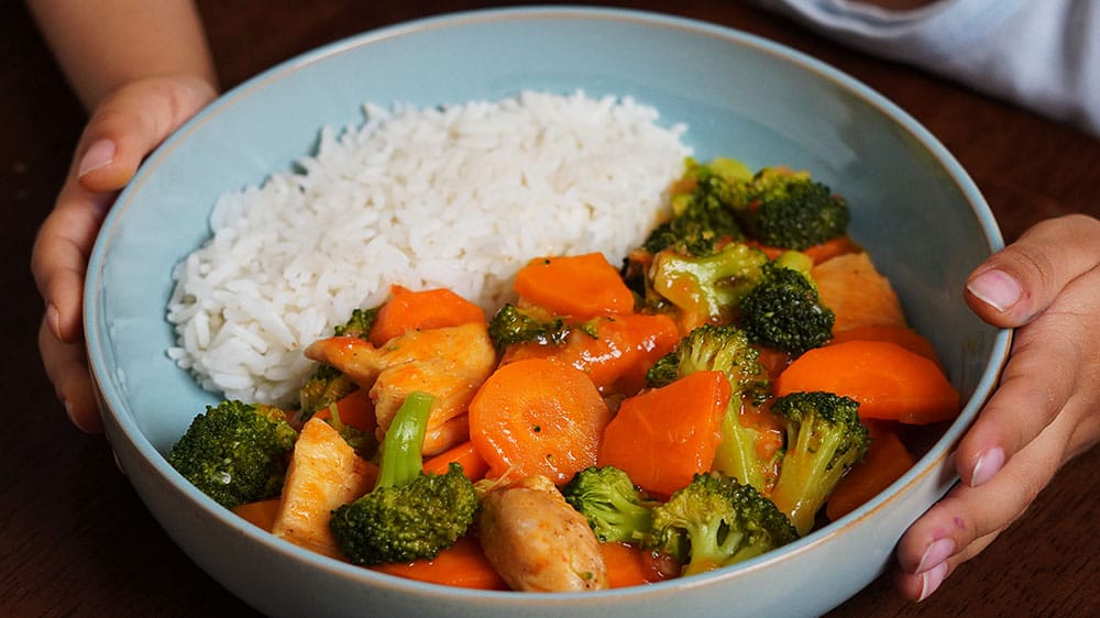 Plato de brócoli con pollo jugoso, acompañado de zanahorias y salsa cremosa, servido con arroz blanco