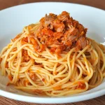 Tallarines rojos con atún, receta peruana casera servida en un plato blanco