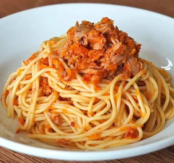 Tallarines rojos con atún, receta peruana casera servida en un plato blanco