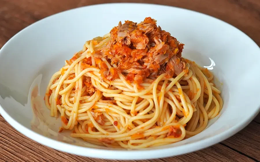 Tallarines rojos con atún, receta peruana casera servida en un plato blanco