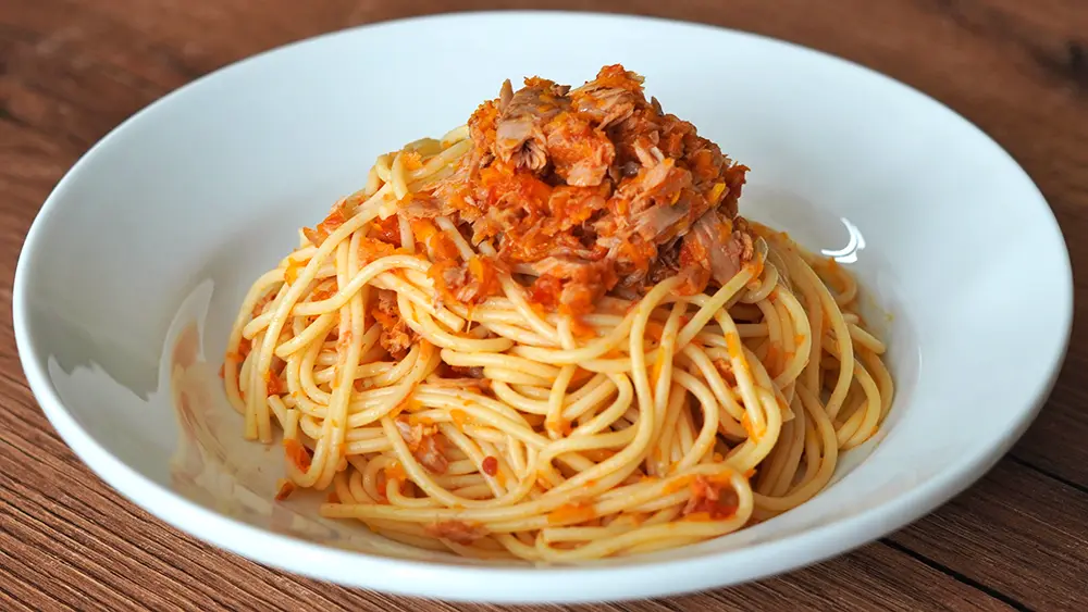 Tallarines rojos con atún, receta peruana casera servida en un plato blanco